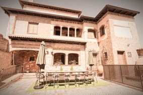 Fachada de piedra y ladrillo de la casa, con la terraza y una mesa larga bajo las sombrillas