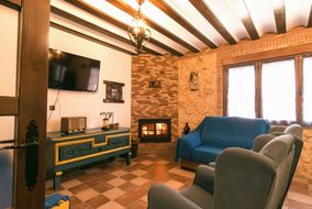 Salón con la chimenea encendida, sofá azul, butacas y techo de vigas de madera